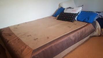 A single bed with a brown and beige bedspread, two pillows, and a blue blanket.