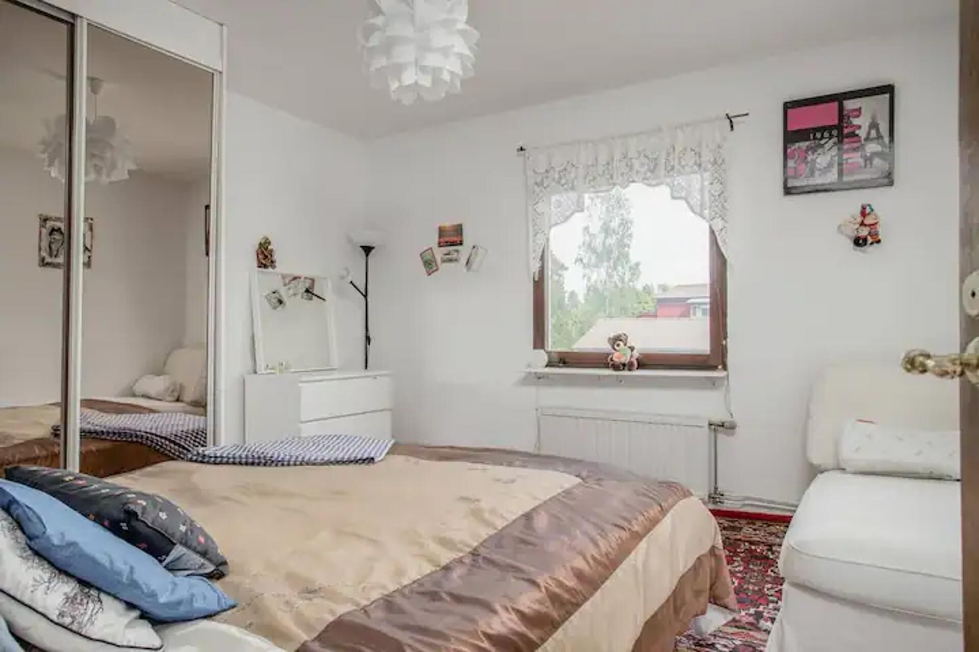 Un dormitorio con cama, armario, ventana con vistas, radiador y una silla.