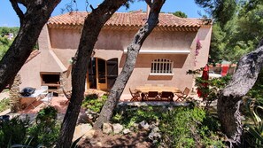 Traditional villa with a spacious patio, stone fireplace, and lush greenery.