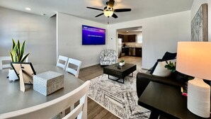 Ein modernes Wohnzimmer mit Flachbildfernseher, Deckenventilator und einer Küche im Hintergrund.