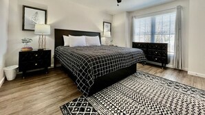Ein Schlafzimmer mit einem Bett, zwei Nachttischen, einem Deckenventilator, einem Fenster mit Vorhängen und einem gemusterten Teppich.