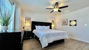 A bedroom with a bed, nightstands, a ceiling fan, and wall art.