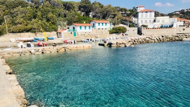 Una zona costera con aguas transparentes, un litoral rocoso y edificios con tejados rojos.