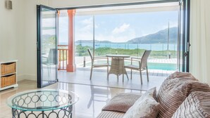 A spacious balcony with a glass door leading to a pool area, wicker furniture, and a view of the sea.