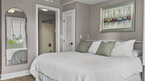 A bedroom with a large bed, a mirror, a door, and a painting on the wall.