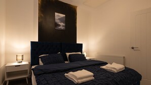 Un lit bien fait, recouvert d’une courtepointe bleu foncé, avec deux serviettes blanches et une tête de lit ornée d’une image de montagnes.