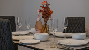 Une table à manger dressée avec de l’assiette blanche, des bols et des verres à vin, ainsi qu’une bouteille de Canti Prosecco et un vase rempli de fleurs séchées.