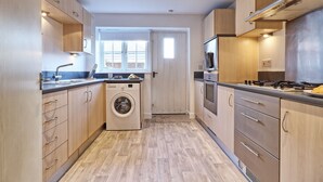 A compact kitchen with wooden cabinets, a built-in washing machine, and a window providing natural light.