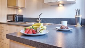 A kitchen with a microwave, sink, and cabinets. There are plates with strawberries and bananas on the counter.