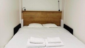 A small, neatly made bed with white linens and two folded towels on the bed. - Stunning 1-bed Studio (Prague)