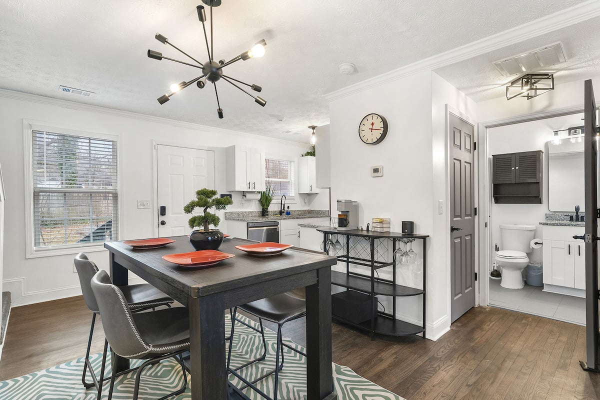 A modern kitchen with white cabinetry, a dining area with a dark table and chairs, and a visible clock on the wall.