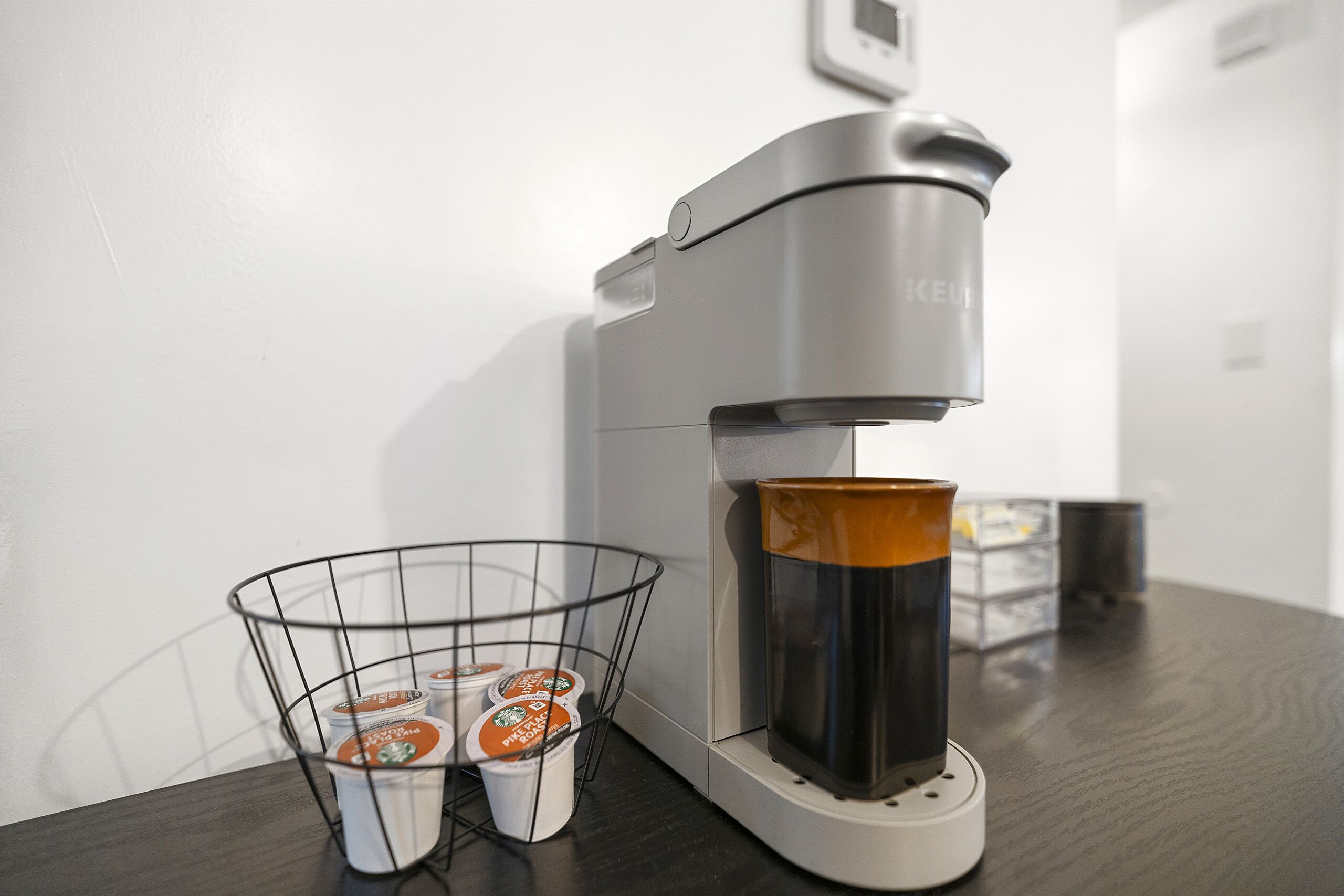 Uma máquina de café com porta-xícaras e um cesto de cápsulas de café.