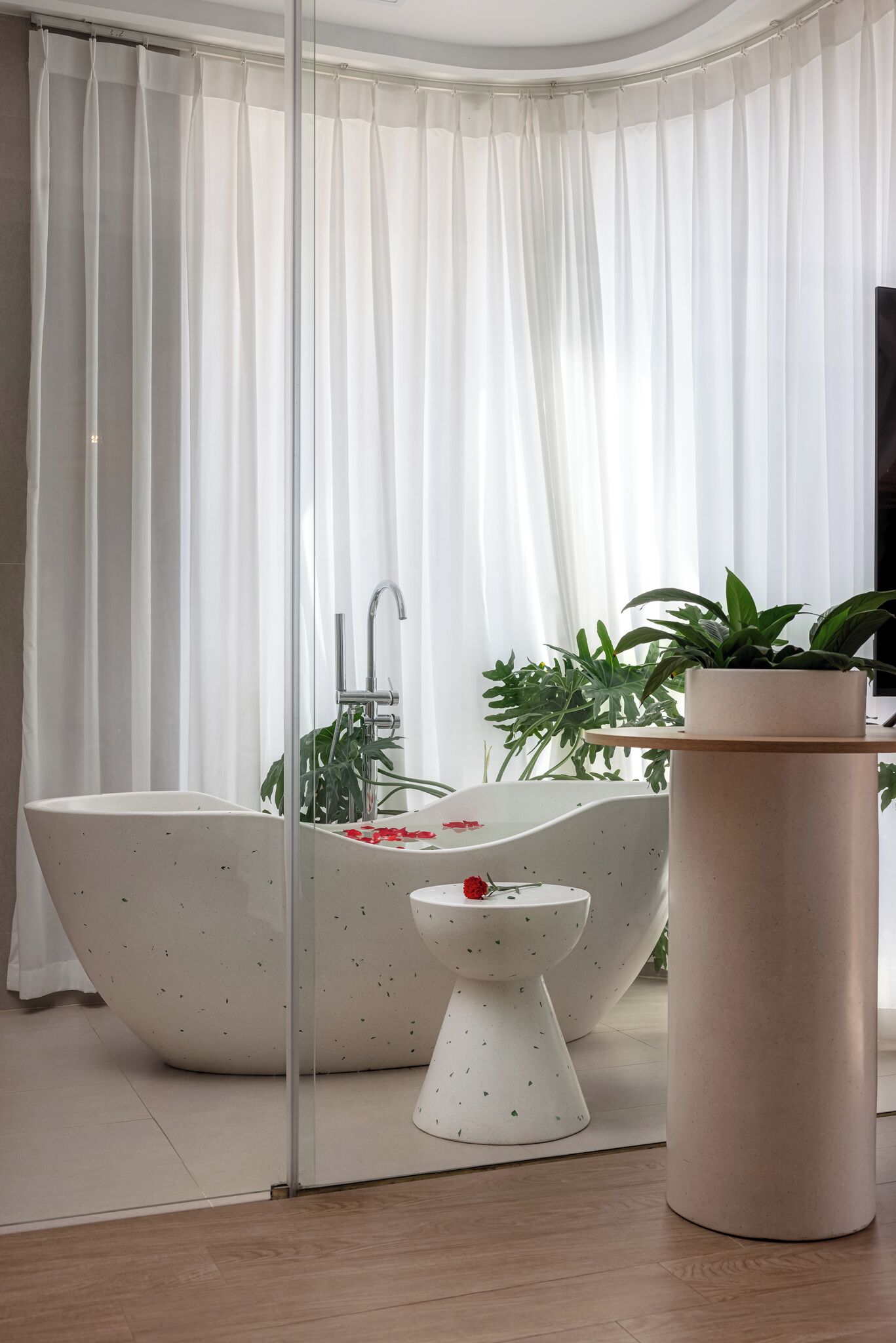 Un baño moderno con una bañera independiente, un lavamanos pequeño blanco y una planta en maceta.