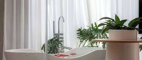 Un baño moderno con una bañera independiente, un lavamanos pequeño blanco y una planta en maceta.