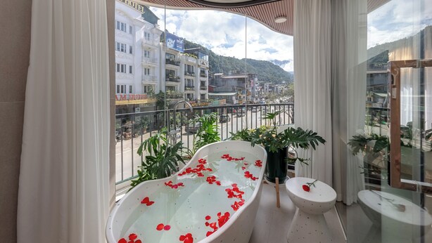 A balcony with a bathtub filled with water and red rose petals, surrounded by potted plants and a small table with a rose. - Tropical Paradise Sapa Hotel (Sa Pa)
