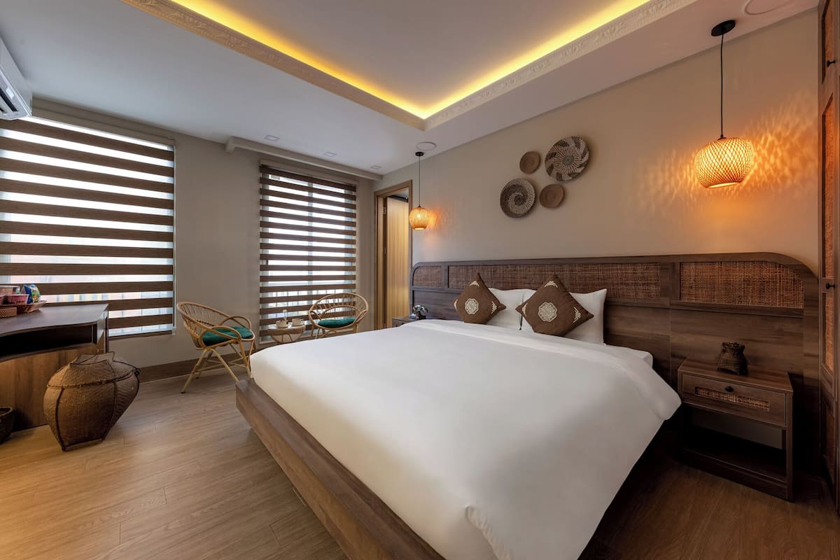 A modern bedroom with a large bed, wooden headboard, bedside tables, and a desk area with a chair.