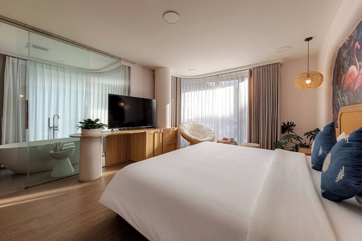 A modern bedroom with a large bed, a television, a desk, and a bathroom with a bathtub and toilet.