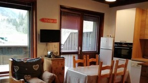 A cozy living room with a wooden sofa, a dining table, and a kitchen area with a refrigerator and oven. - 50m from ski lifts, 1st floor, terrace, parking, tv, 30m², Arêches-Beaufort (Beaufort)