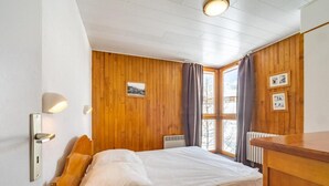 A bedroom with a wooden bed, a nightstand, a radiator, and a window with curtains.