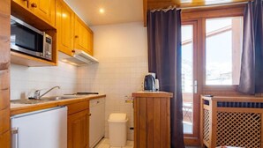 A compact kitchen with wooden cabinets, a microwave, a sink, and a small trash bin.