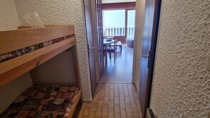 Un couloir étroit, avec un lit superposé sur le côté gauche et une porte donnant sur un balcon.