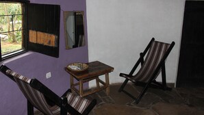 A room with two striped chairs, a small wooden table with a woven basket, and a window with a metal grill. - Red Rocks Rwanda - Campsite & Guesthouse (Nkotsi)