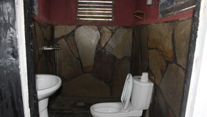 A small, stone-walled bathroom with a toilet, sink, and shower. - Red Rocks Rwanda - Campsite & Guesthouse (Nkotsi)