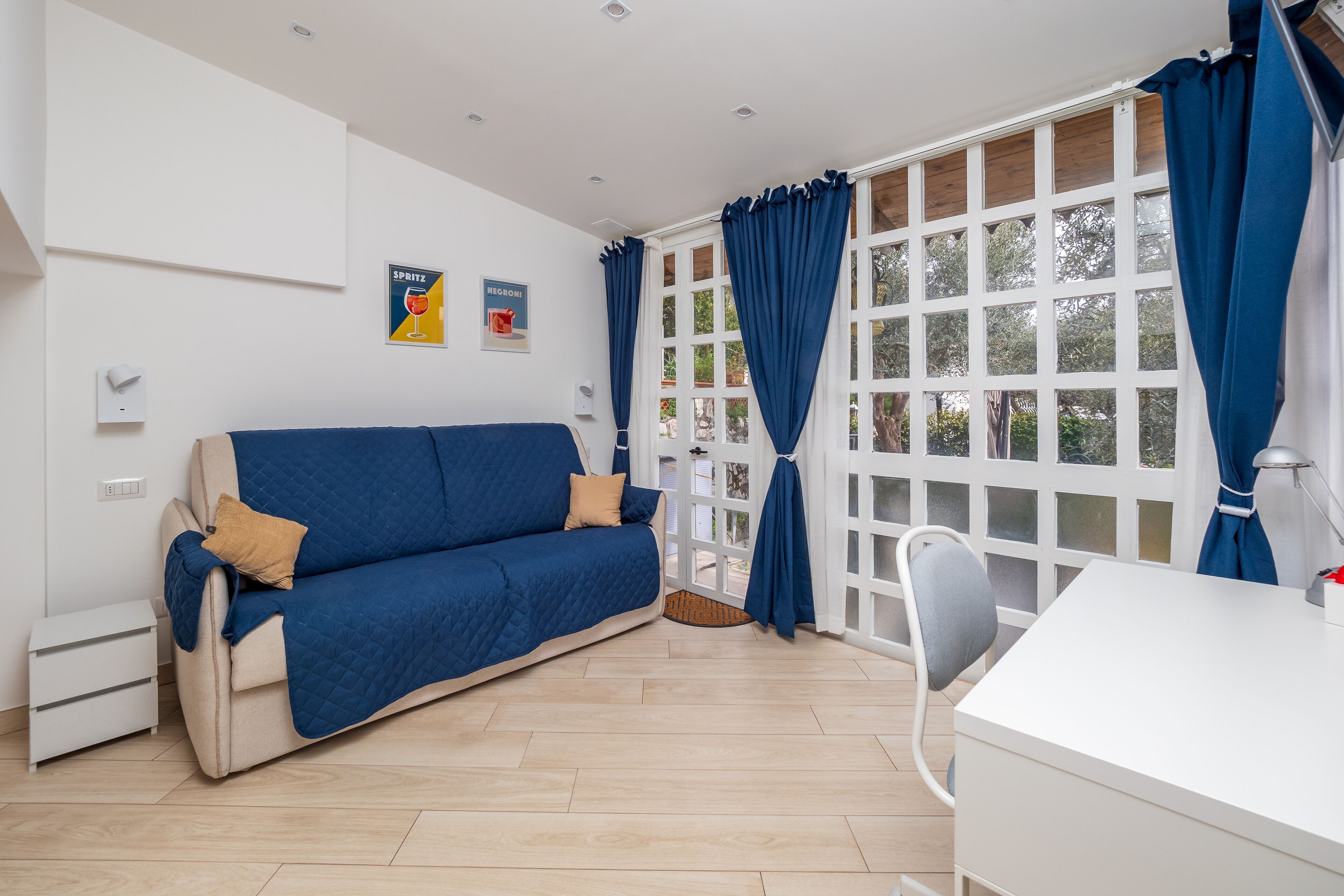 A modern room with a blue sofa, a white desk, and large windows with blue curtains.