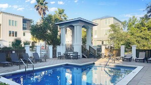 A swimming pool with lounge chairs and a covered seating area, surrounded by buildings and greenery. - Remodeled 5 bedroom house with bikes – walking distance to the beach  (Santa Rosa Beach)