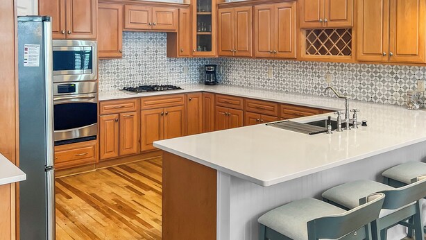 A modern kitchen with wooden cabinets, a central island with bar stools, stainless steel appliances, and pendant lighting. - Remodeled 5 bedroom house with bikes – walking distance to the beach  (Santa Rosa Beach)