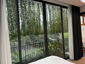 A bedroom with a large sliding glass door leading to a balcony with a view of a lush garden.