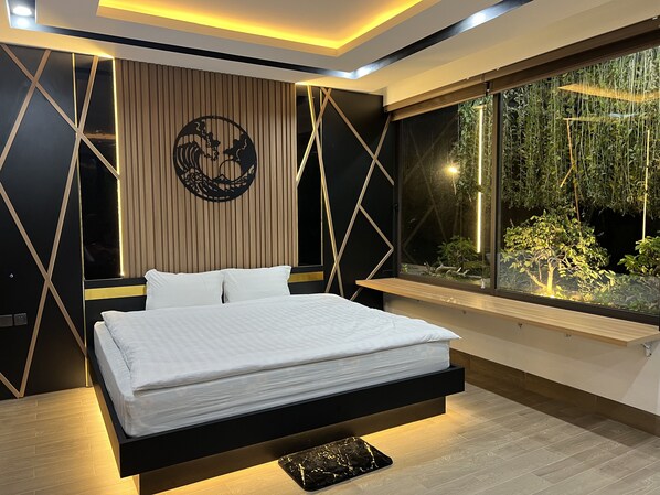 A modern bedroom with a bed, a large window with a view of greenery, and geometric wall designs.
