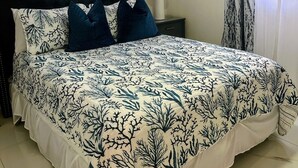 A bedroom with a large bed, dark headboard, and patterned bedspread. There is a nightstand with a lamp and a framed picture on the wall. - K&L Villa Apartment (Christ Church)