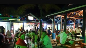 A crowded outdoor dining area with wooden tables and benches, surrounded by buildings with visible signage. - K&L Villa Apartment (Christ Church)