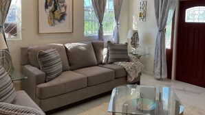 A living room with a beige sofa, a glass coffee table, and a framed abstract painting on the wall. - K&L Villa Apartment (Christ Church)
