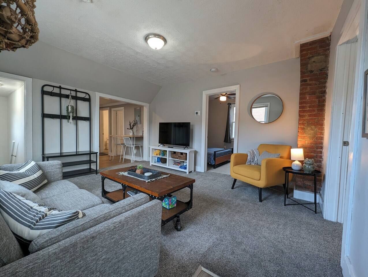 Ein Wohnzimmer mit Sofa, Sesseln, Couchtisch, Fernseher und einer Wand aus Ziegelsteinen.