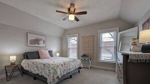 Une chambre à coucher comprenant un lit, un ventilateur de plafond, une commode et une fenêtre avec des stores.