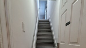 Un couloir étroit avec un escalier recouvert de moquette menant à une porte sur laquelle est apposée une pancarte.