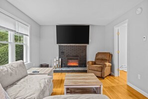 A living room with a fireplace, a sofa, a coffee table, and a television mounted above the fireplace. - Charming 5B Home in Neighborhood (South Burlington)