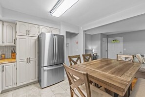 A modern kitchen with white cabinetry, a stainless steel refrigerator, and a wooden dining table with chairs. - Charming 5B Home in Neighborhood (South Burlington)