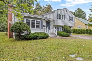 A two-story house with a front porch, a brick chimney, and a well-maintained lawn. - Charming 5B Home in Neighborhood (South Burlington)