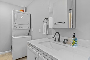 A modern bathroom with a built-in washer and dryer, a large mirror, a sink with a black faucet, and a bottle of hand soap. - Charming 5B Home in Neighborhood (South Burlington)