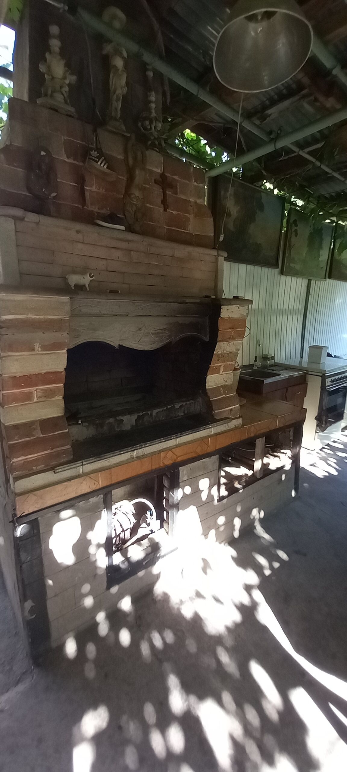 Un horno de ladrillo al aire libre con un estante superior, un colgador para ollas y una ventana a la derecha.