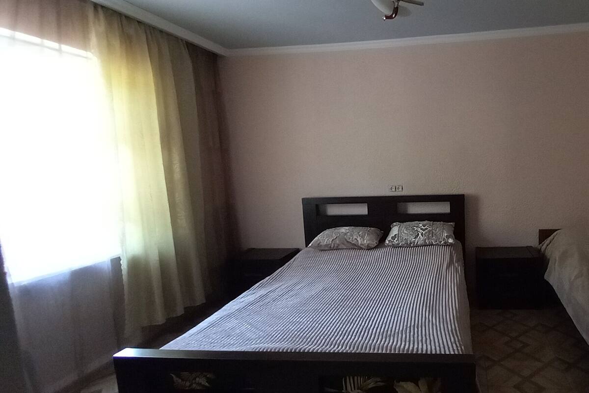 A single bed with a headboard, a bedside table, and a window with curtains.