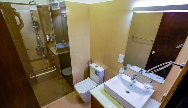 A bathroom with a glass-enclosed shower, a toilet, and a sink with a mirror above it.