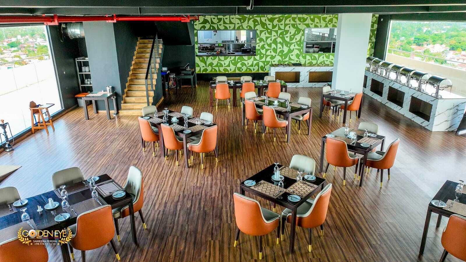 A restaurant with multiple dining tables and chairs, a kitchen area, and a staircase leading to an upper level.