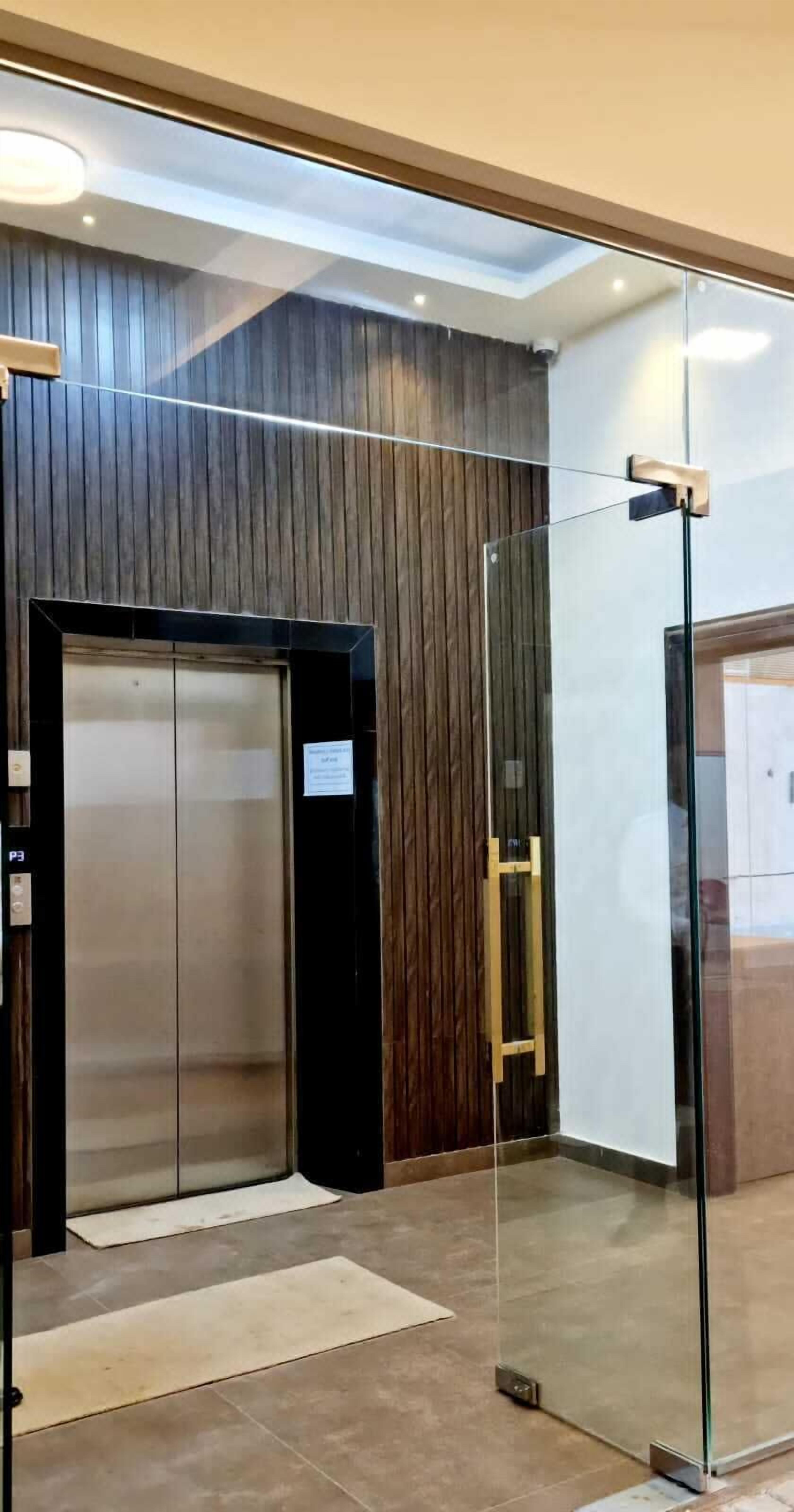 Ein moderner Aufzug mit Glastür, Holzverkleidung und Metallhandlauf.