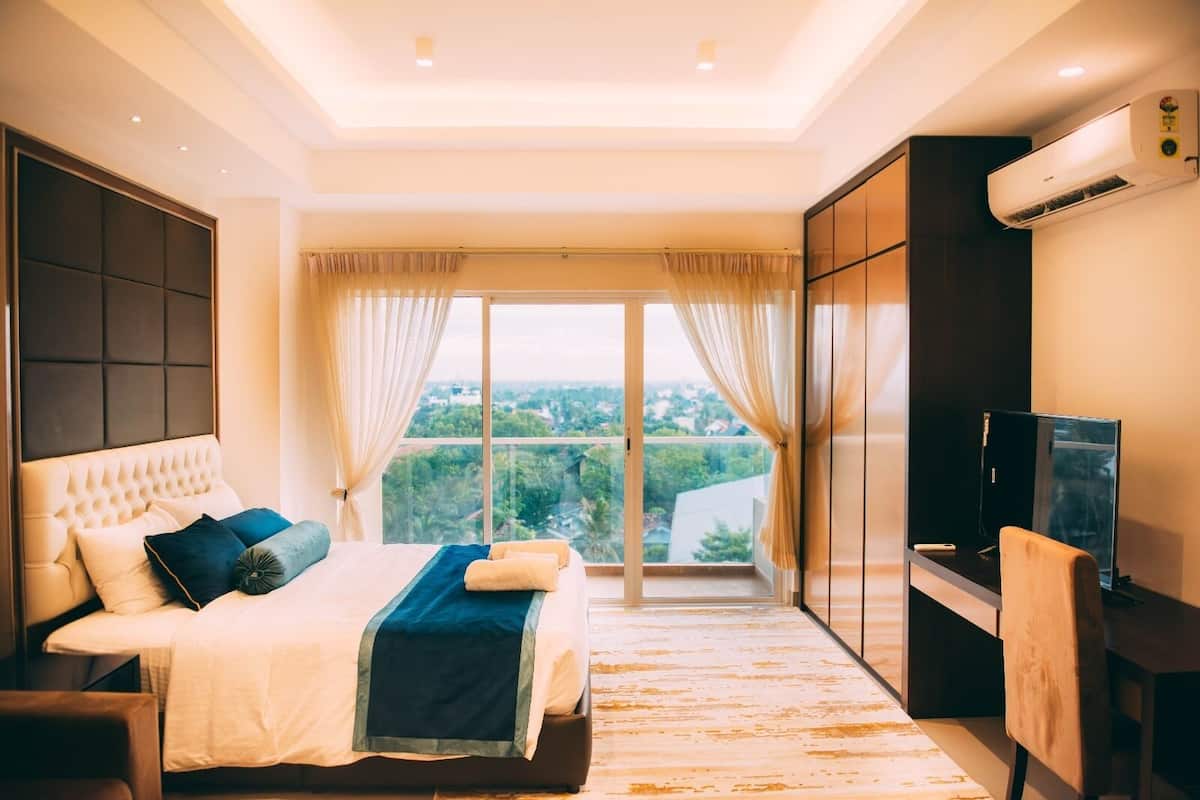 Ein modernes Schlafzimmer mit einem großen Bett, einem Fernseher und Blick auf Grün durch das Fenster.