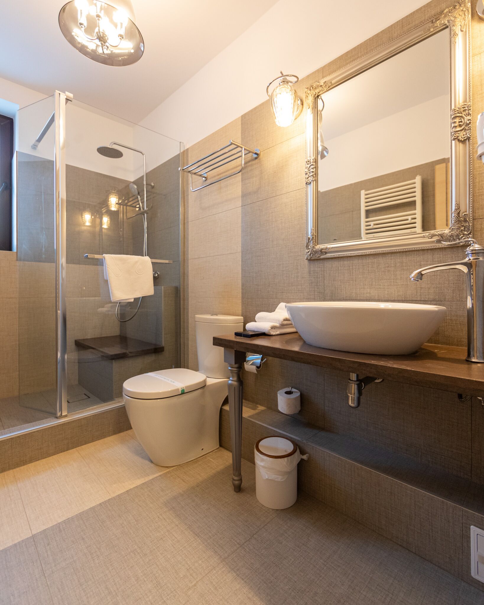 Un bagno moderno con doccia vetrata, un water bianco, un lavandino capiente e uno specchio con cornice decorata.