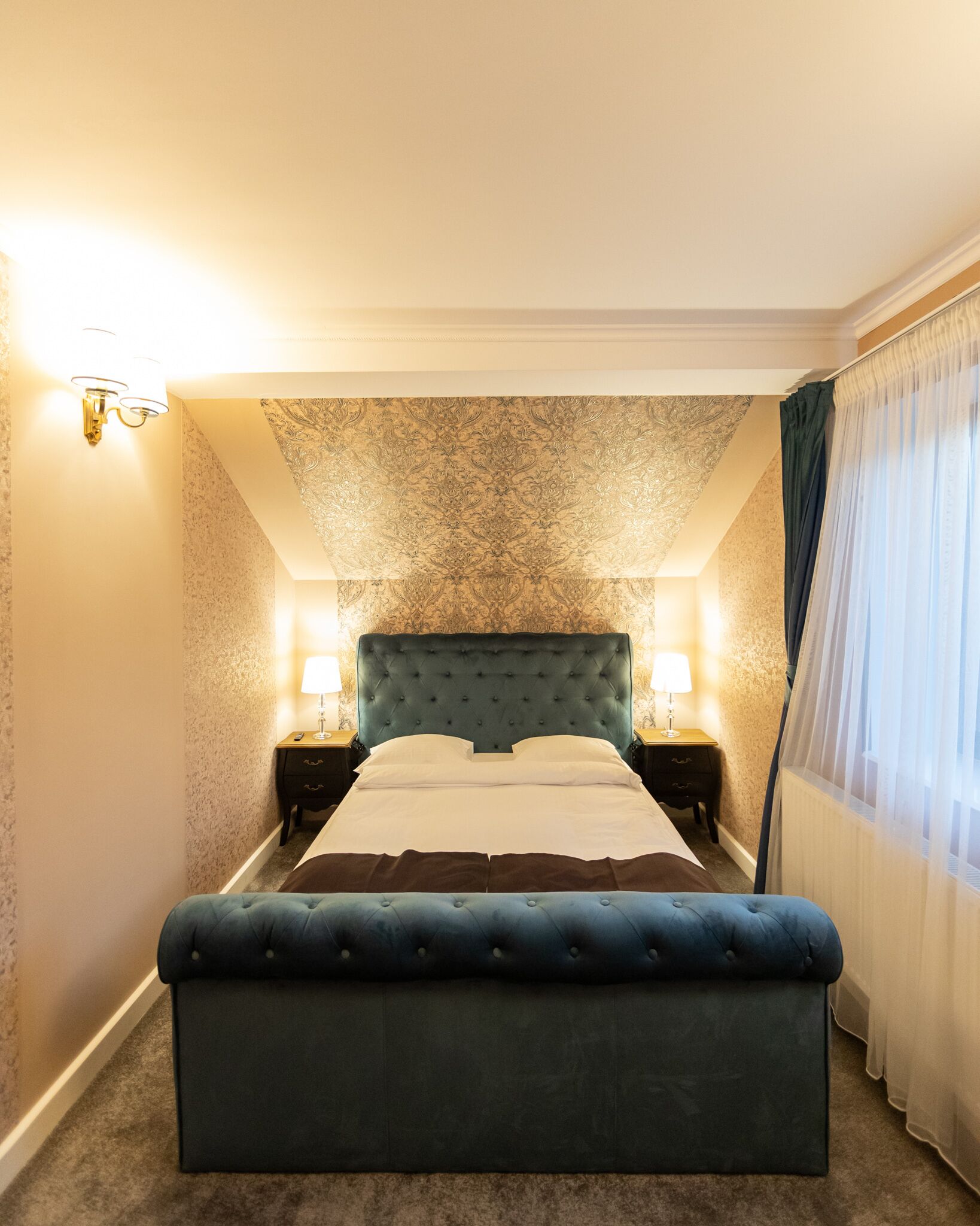 Un dormitorio ordenado con una cama grande, dos mesitas de noche con lámparas y un techo decorativo.